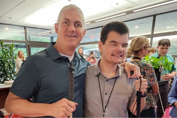 Rich standing next to Level Up volunteer and Envision employee Andy, both are smiling at the camera as they hold their white canes.