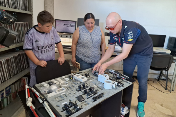 Paco showing two people a table full of low vision technology.